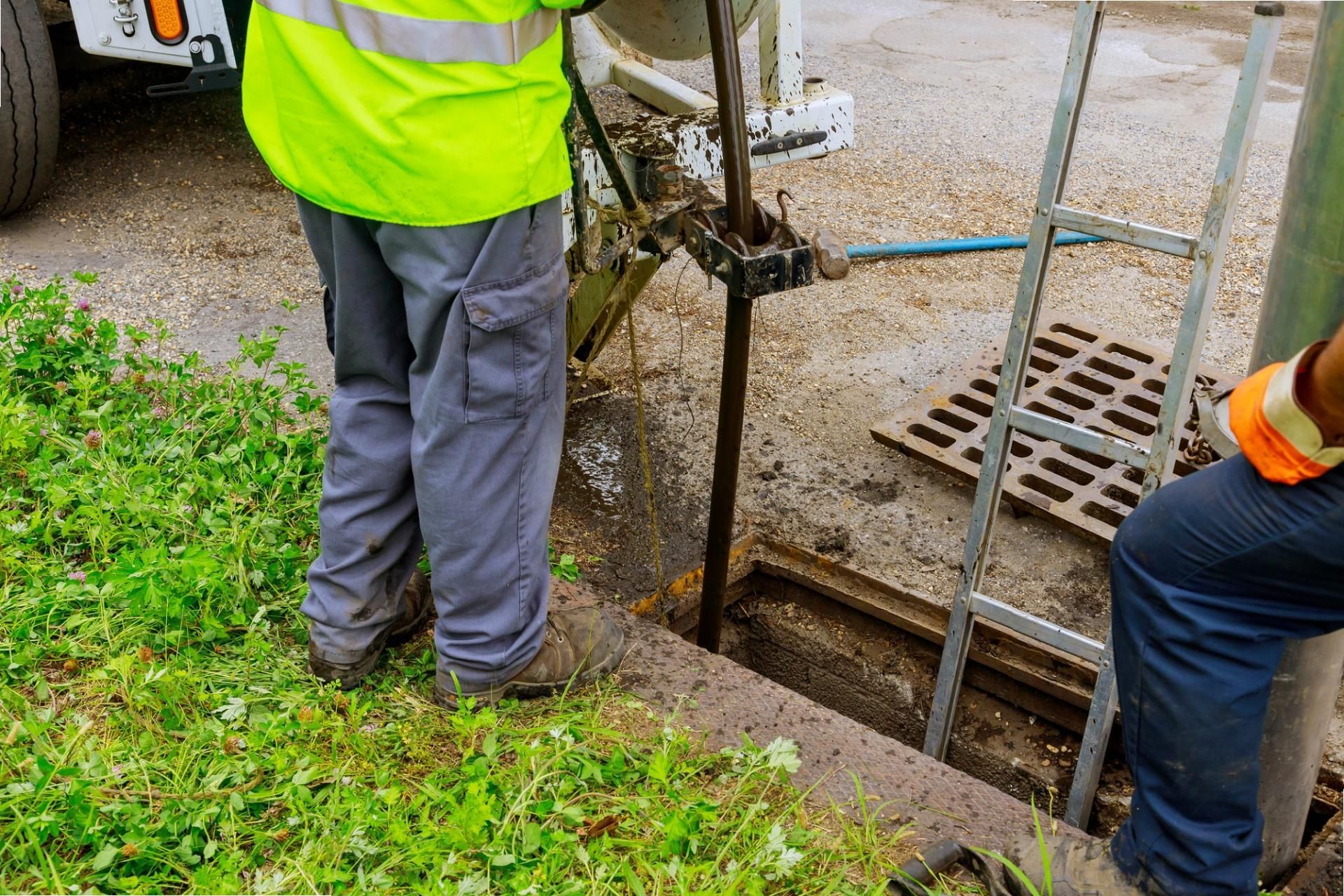 Workers in safety vests beside an open trench near a storm drain grate
