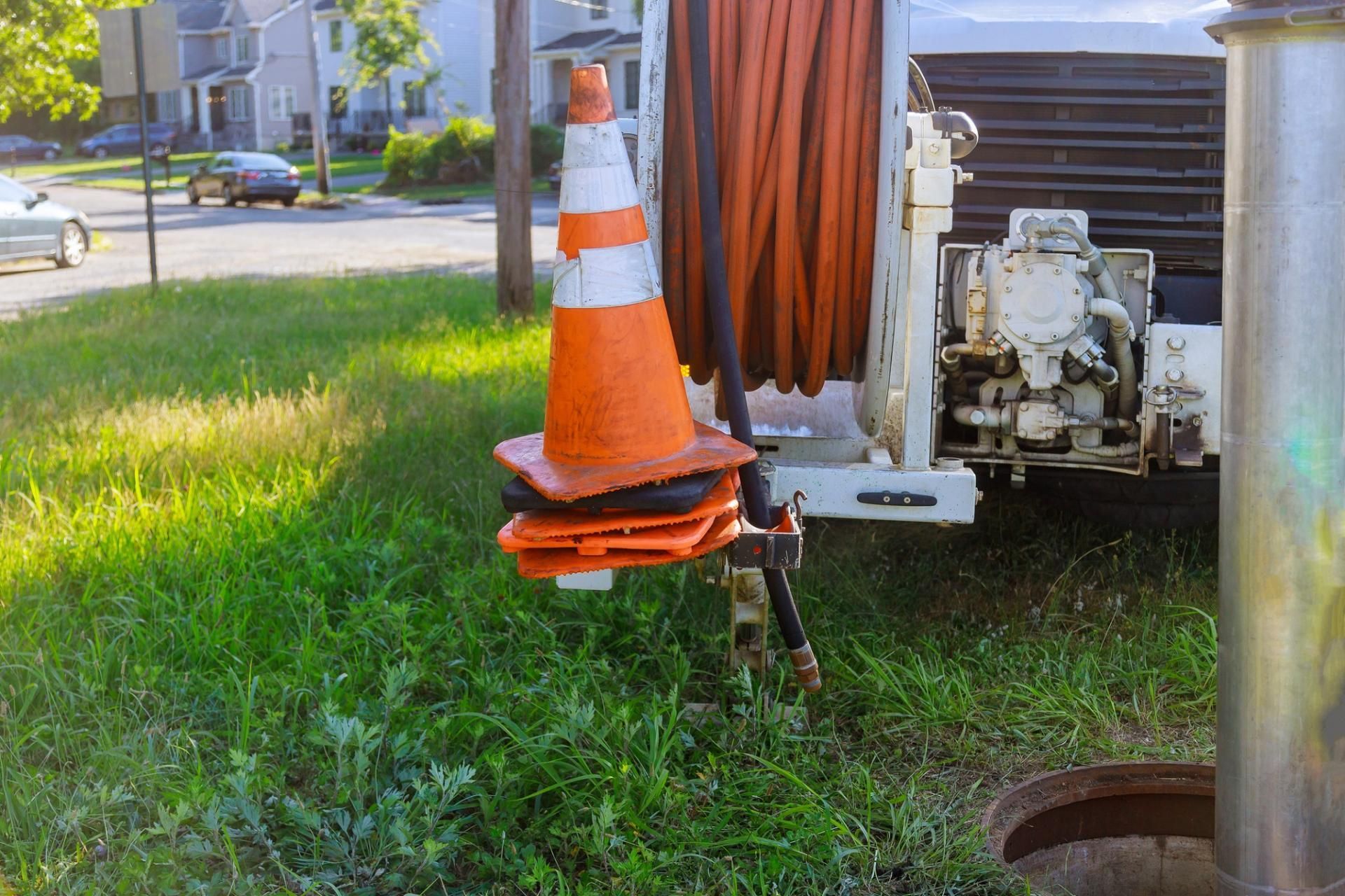 Orange traffic cone on a cable reel truck in a grassy residential area.