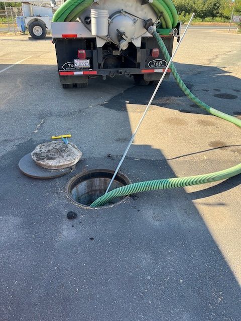 Sewer vacuum truck pumping from an open manhole, with green hose on pavement.
