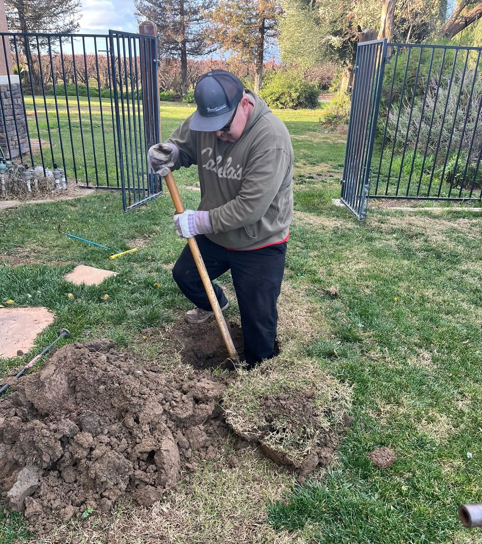 Person digging a hole with a shovel beside a large mound of dirt in a grassy yard.