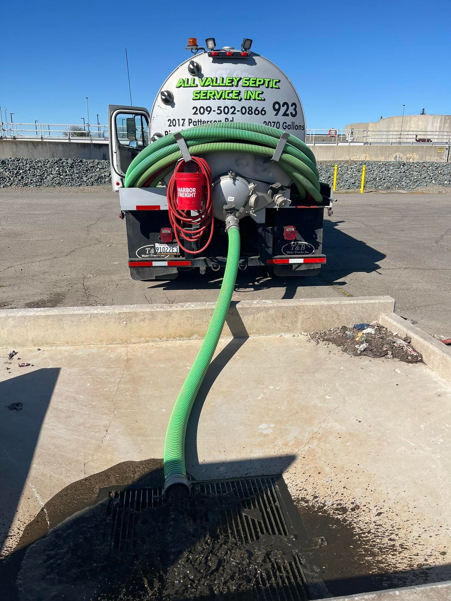 Sewer vacuum truck pumping black sludge into a concrete pit at a harbor