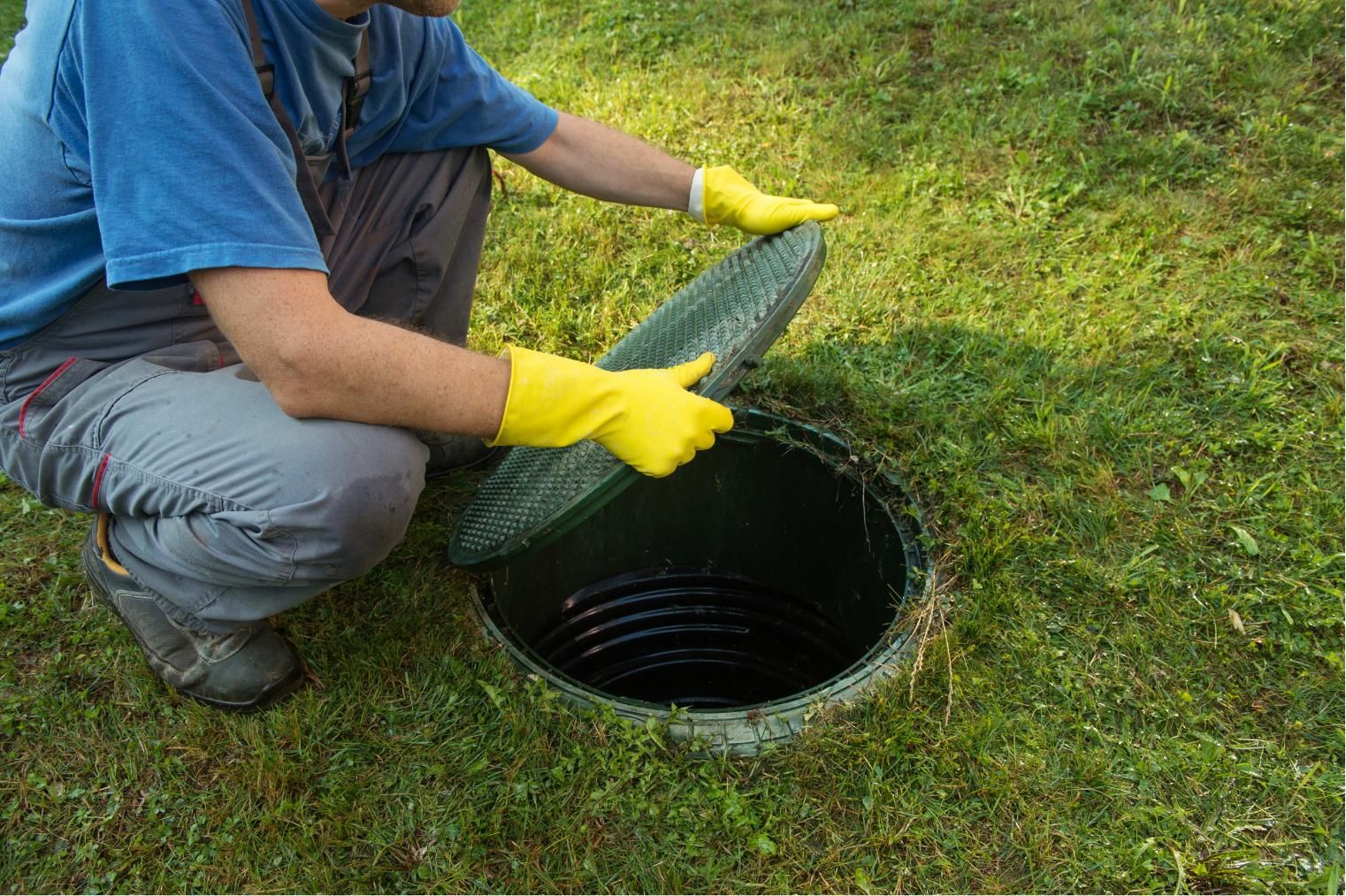 Person in blue shirt and yellow gloves placing a cover over an open outdoor drain in the grass