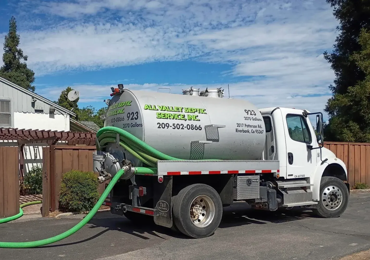White vacuum truck with green hose pumping in a residential street under a blue sky