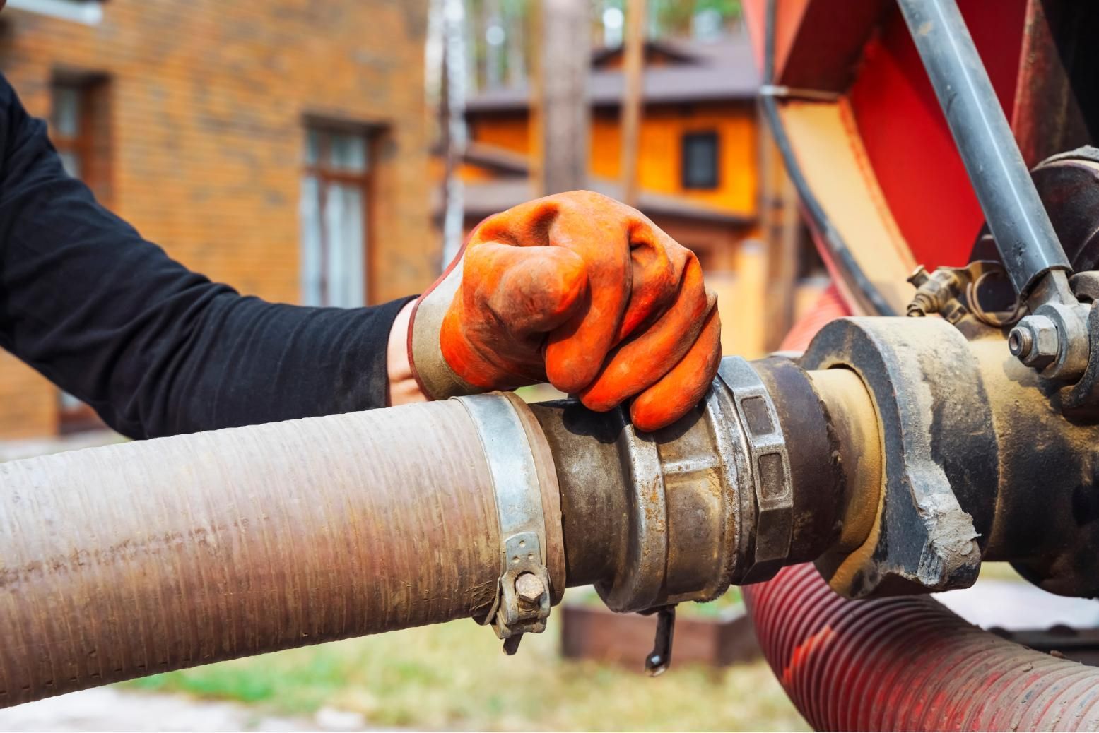 Gloved hand tightening a metal hose coupling on a pipe outdoors
