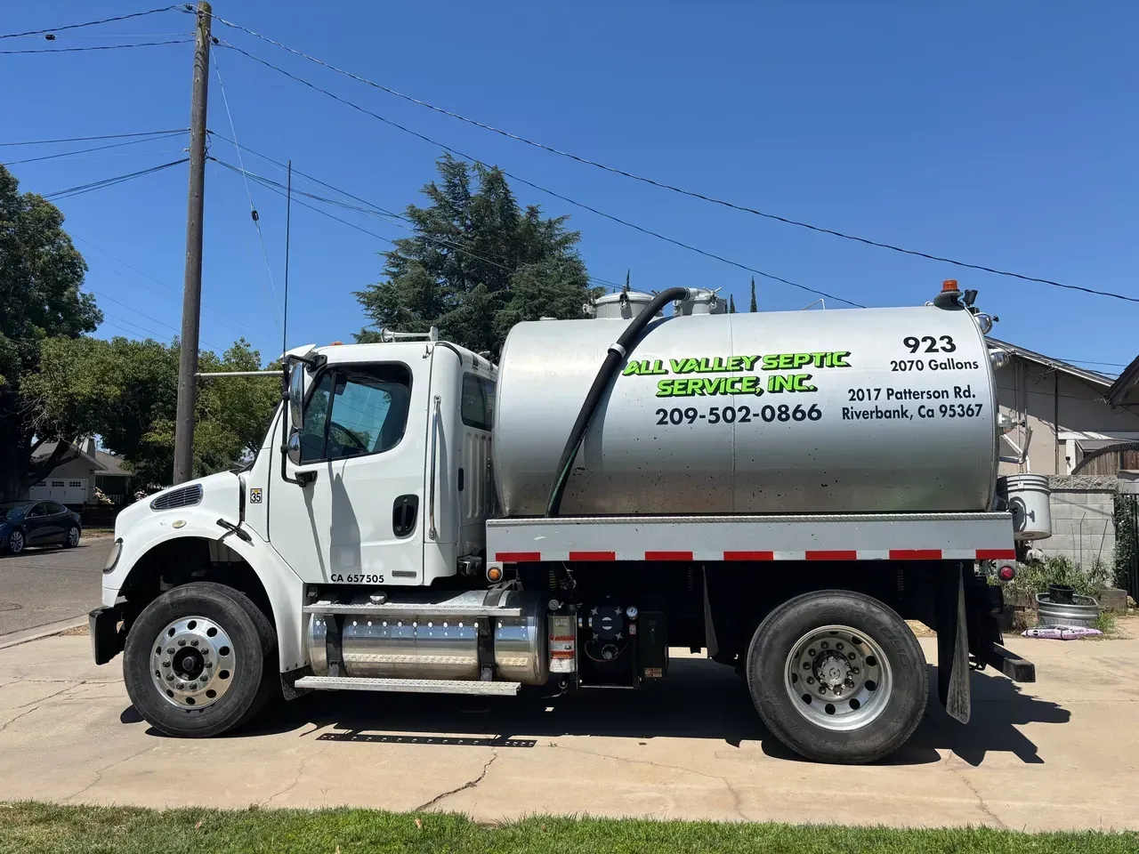 White tanker truck parked on a street under a blue sky, with company lettering on the tank.