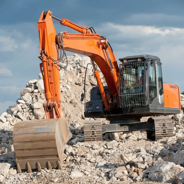Orange excavator on a rubble pile at a demolition site under cloudy skies