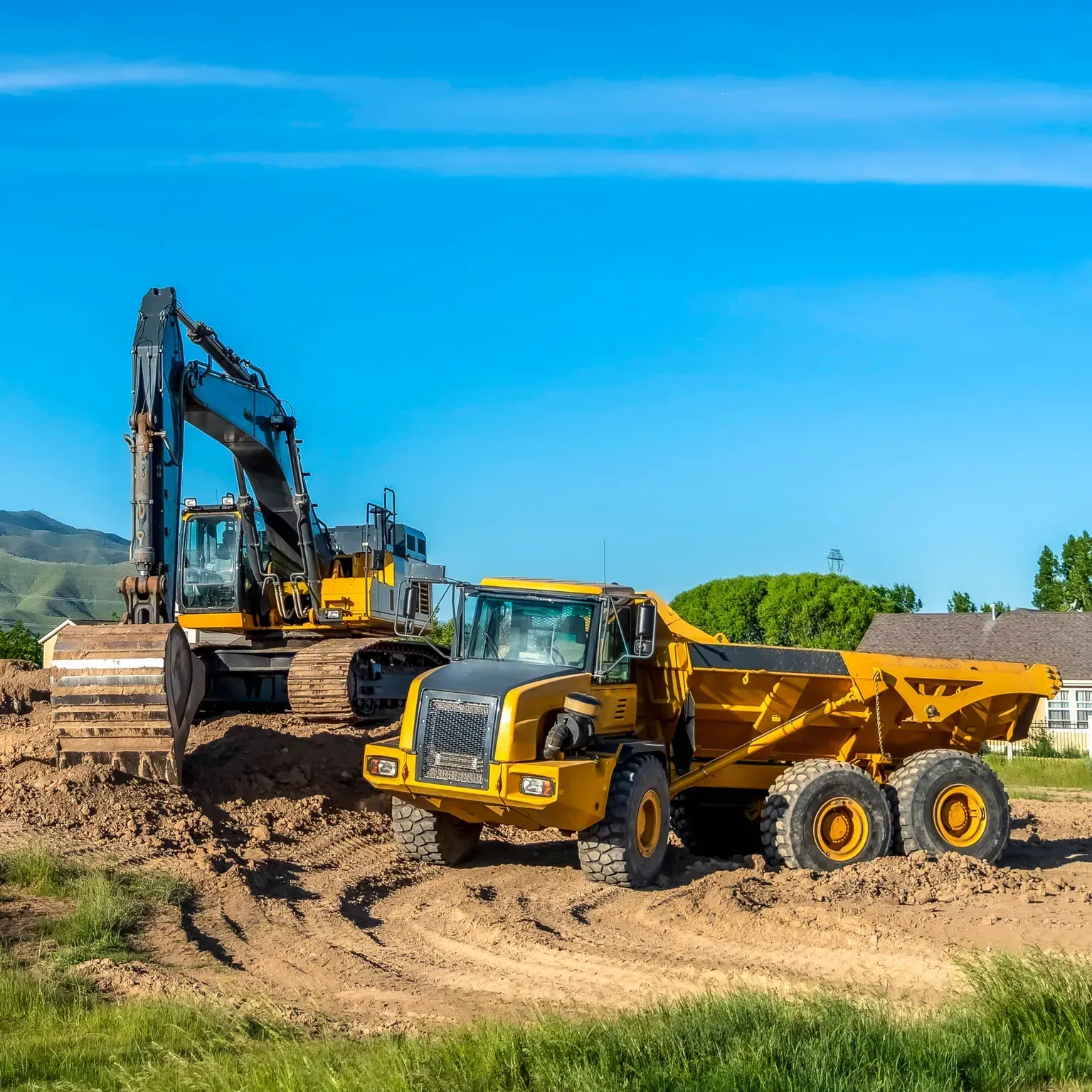 Yellow dump truck and excavator working on a dirt site under a blue sky