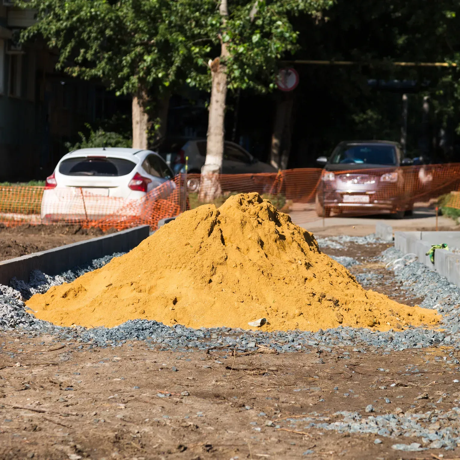 Yellow sand pile on a construction site beside parked cars and trees