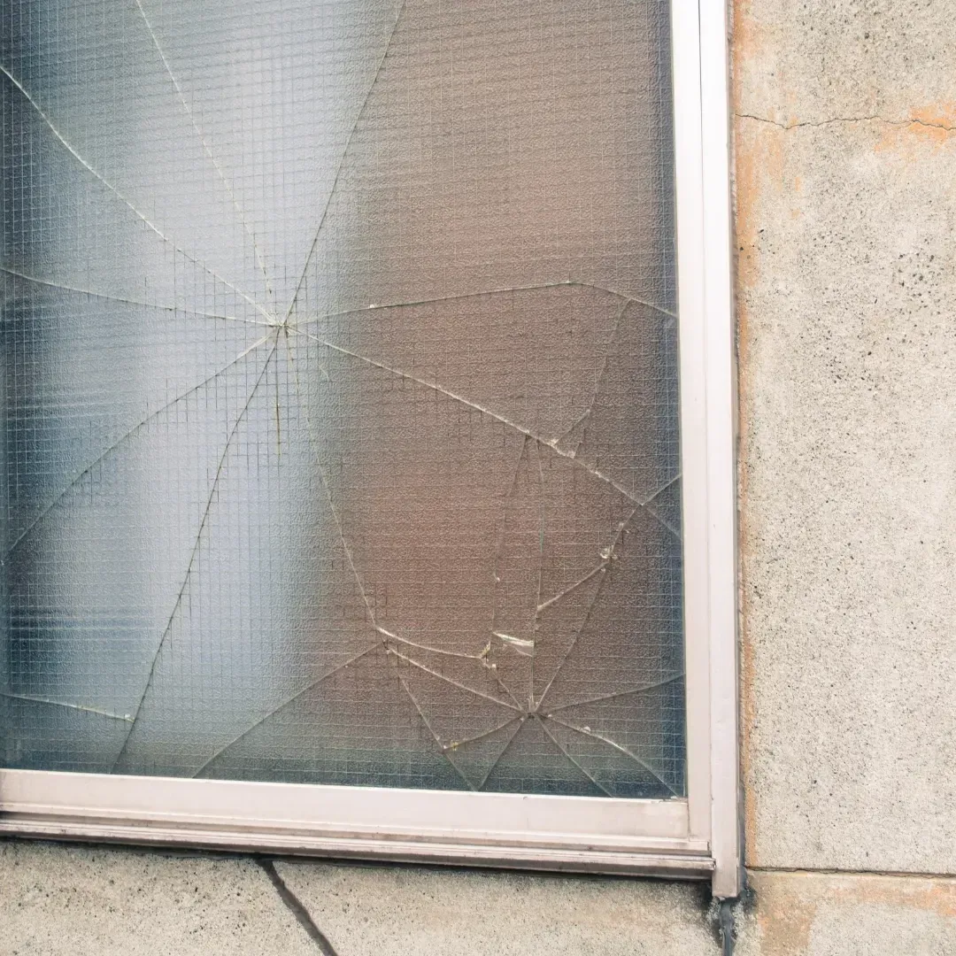 Cracked frosted windowpane in a white frame beside a beige wall