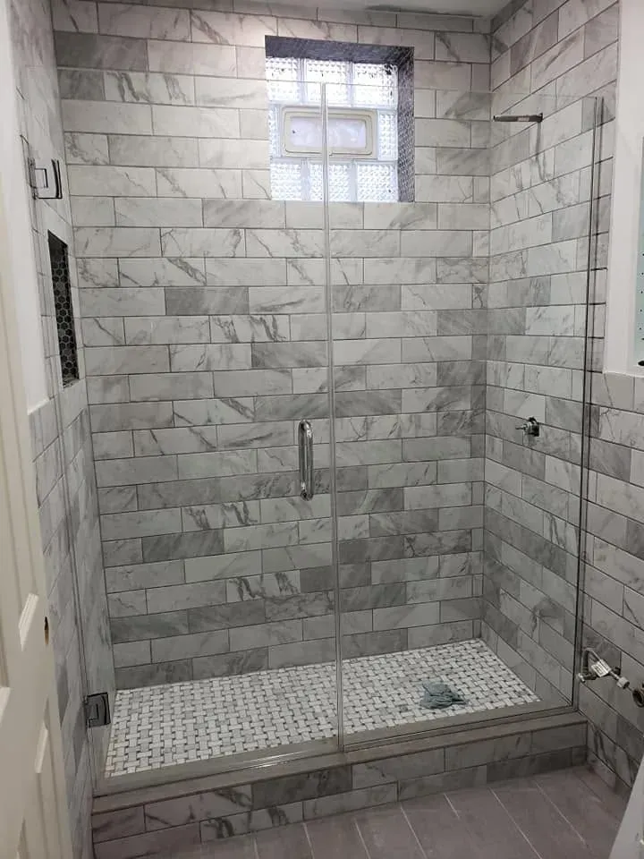 Frameless glass shower enclosure with marble-look tile and chrome hardware in a bathroom in Addison