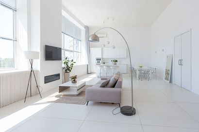 Bright minimalist living room with white walls, gray sofa, large windows, and modern floor lamp