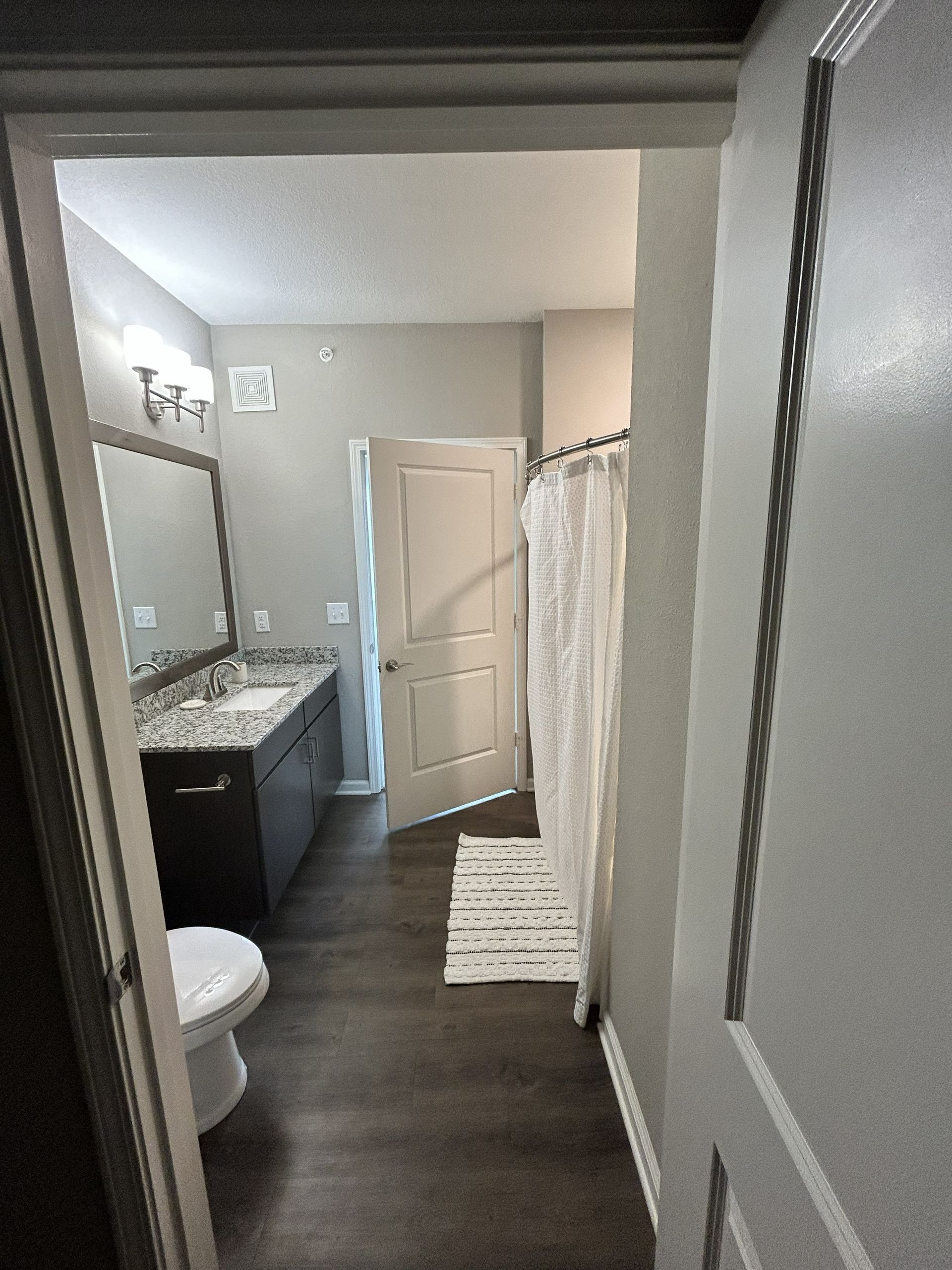 Bathroom interior with double vanity, mirror, shower curtain, and open door view from the hallway