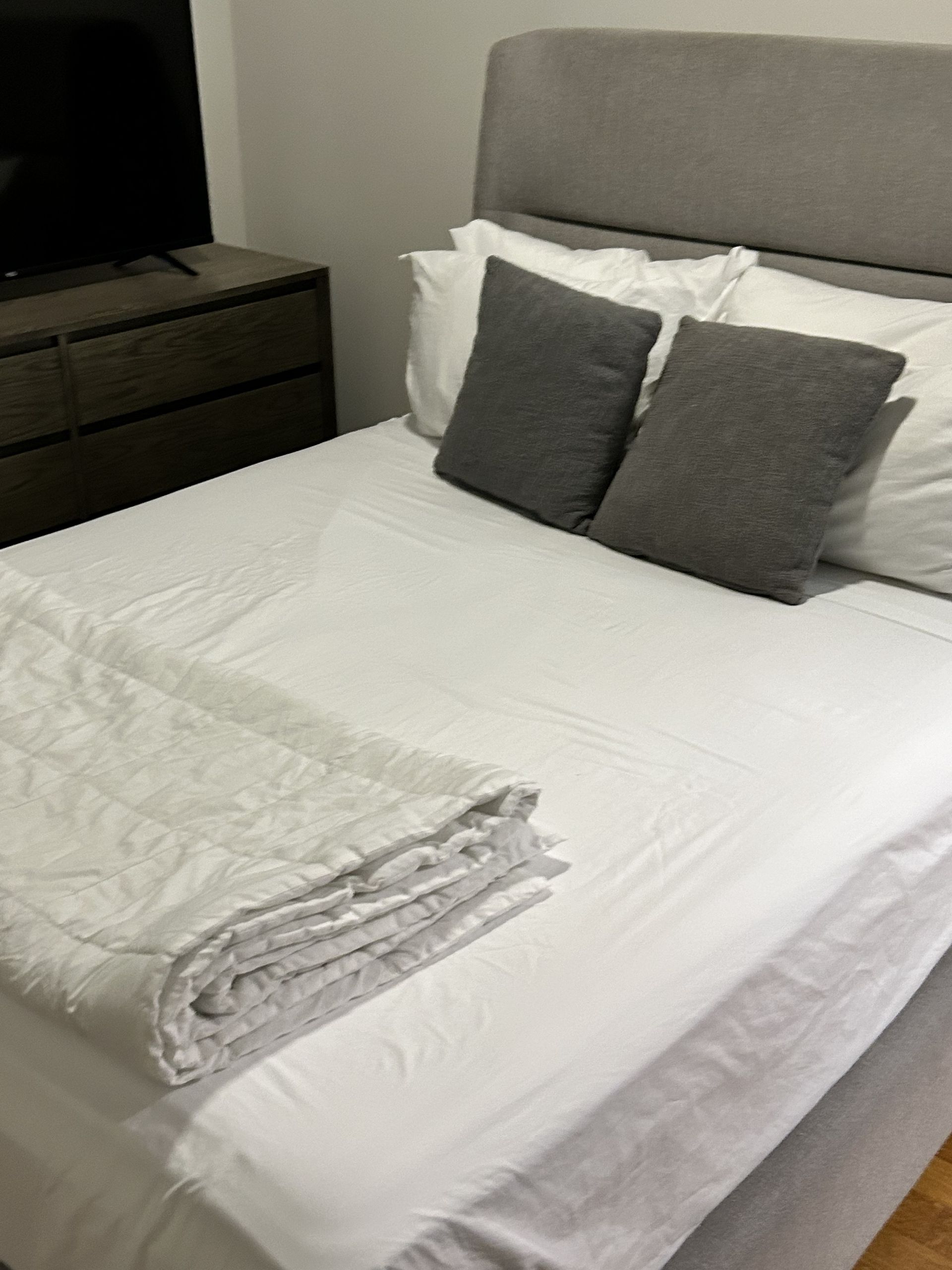 Neatly made bed with white bedding, gray pillows, and a folded towel at the foot in a bedroom