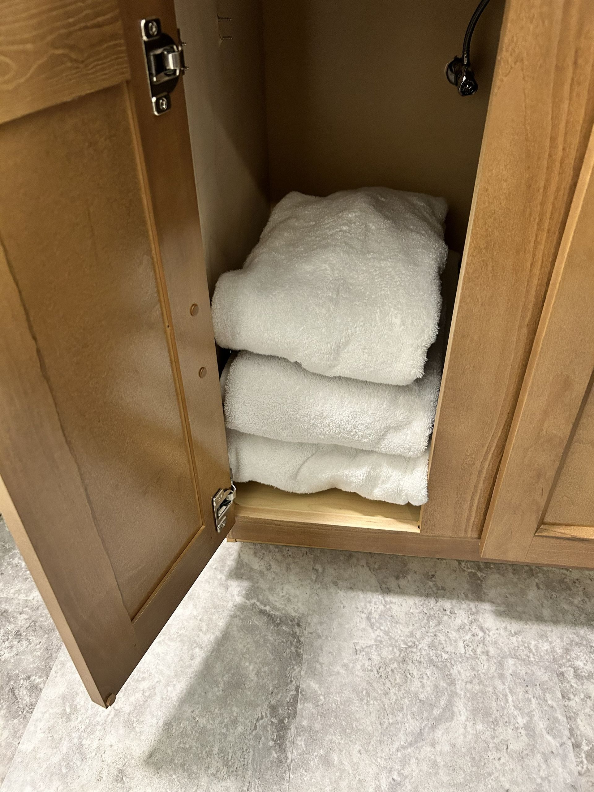 Open cabinet with stacked white towels inside and a gray carpet below