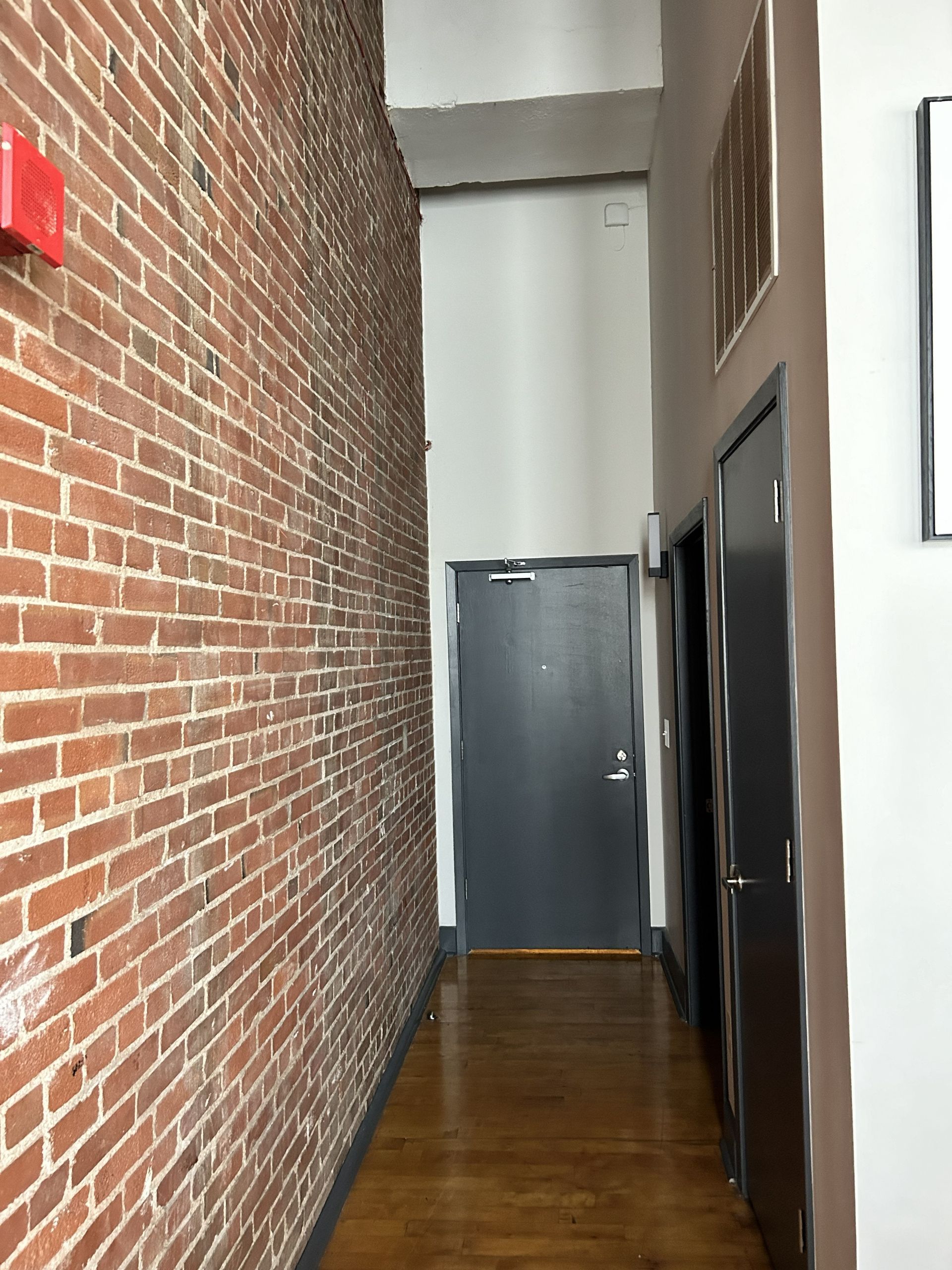 Narrow hallway with brick wall, wood floor, and gray doors at the end
