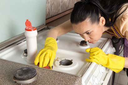 Person using a handheld vacuum to clean a gray ottoman indoors