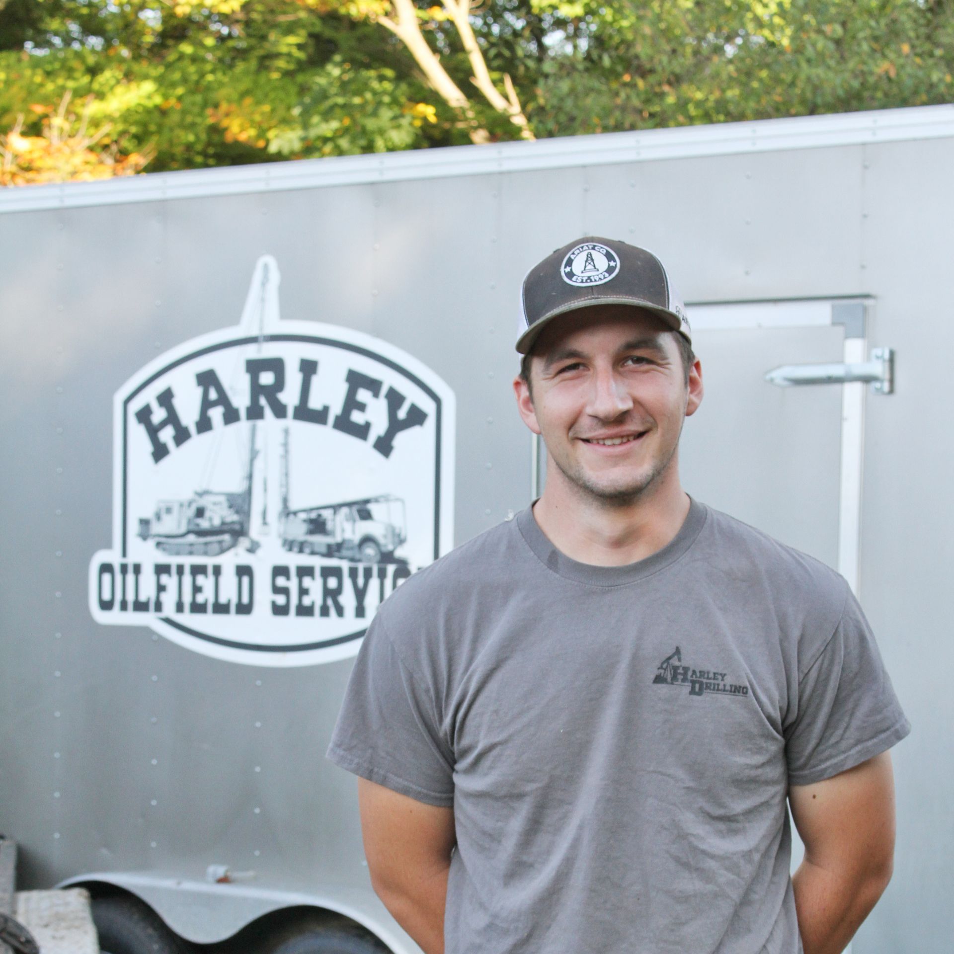 Man in cap and t-shirt smiles in front of trailer with 