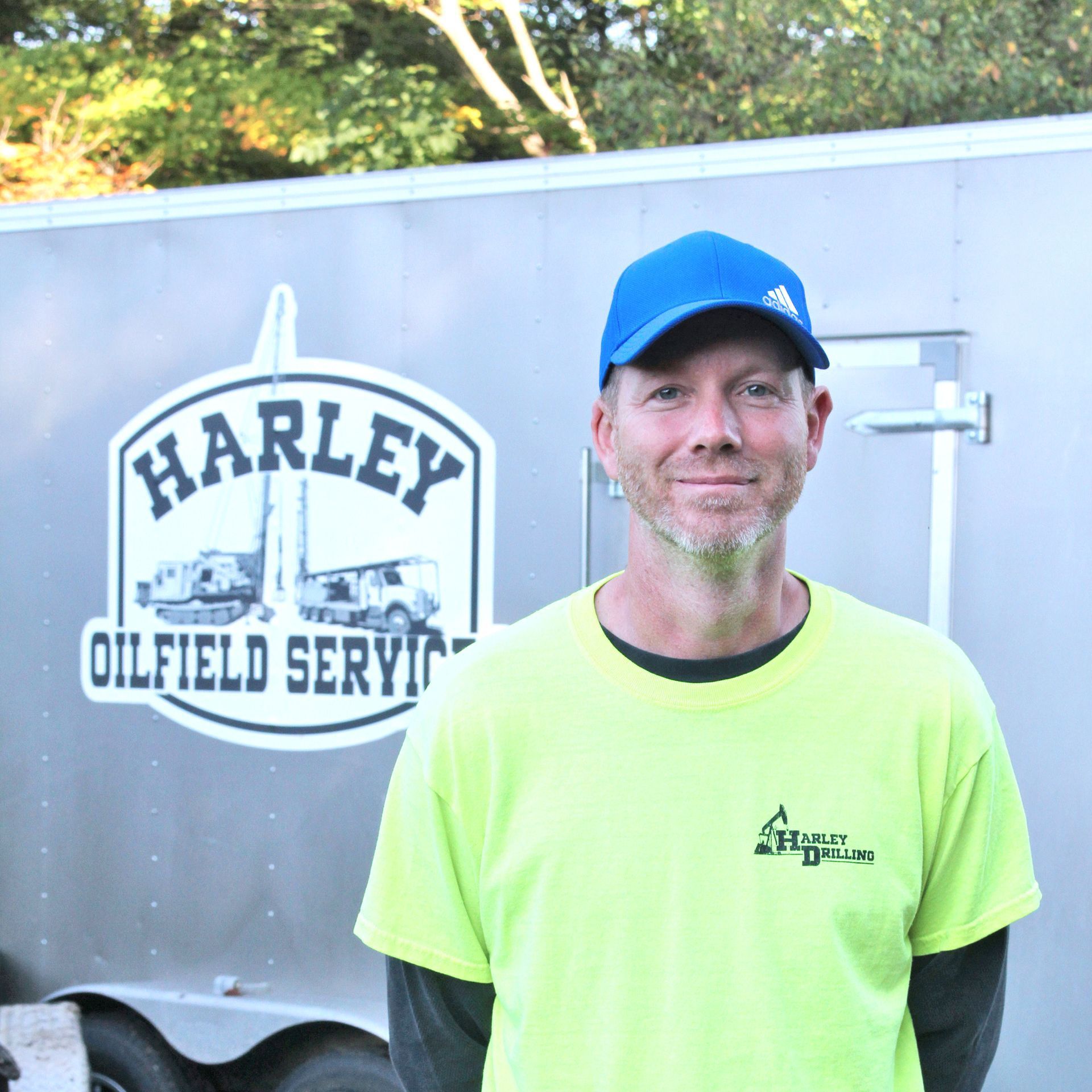 Man in blue cap and neon shirt in front of a trailer with 