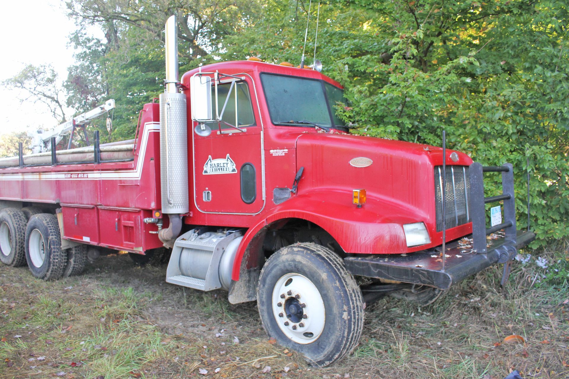 Red Peterbilt flatbed truck parked on grass near trees.