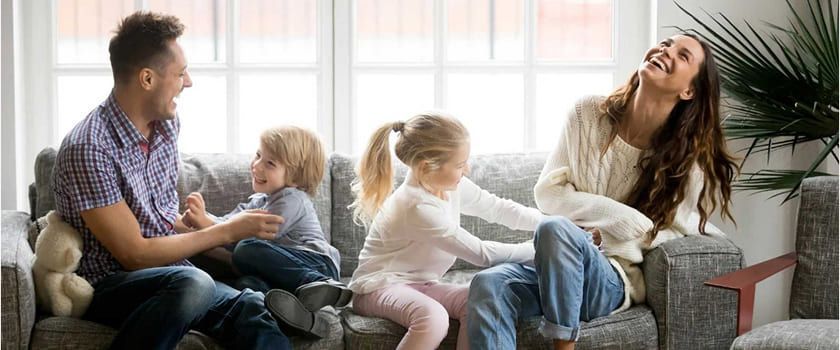 Family laughing together on a couch near a window. 