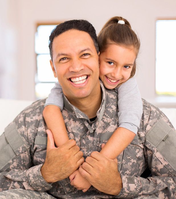 A smiling soldier in camouflage uniform being hugged from behind by a child. A smiling soldier in camouflage uniform being hugged from behind by a child.