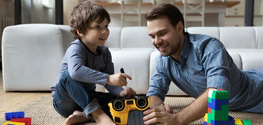 A man and a child playing with toys on the floor near a couch. A man and a child playing with toys on the floor near a couch.