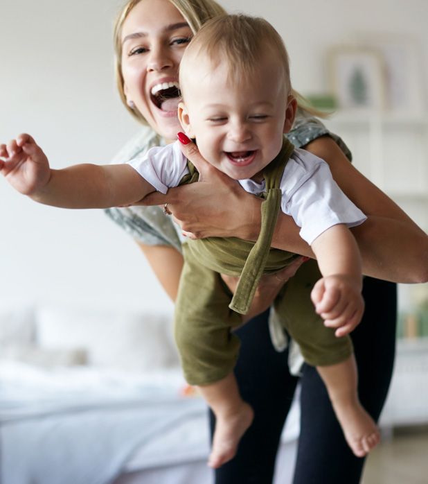 Woman holding a laughing baby wearing green overalls and a white shirt. Woman holding a laughing baby wearing green overalls and a white shirt.