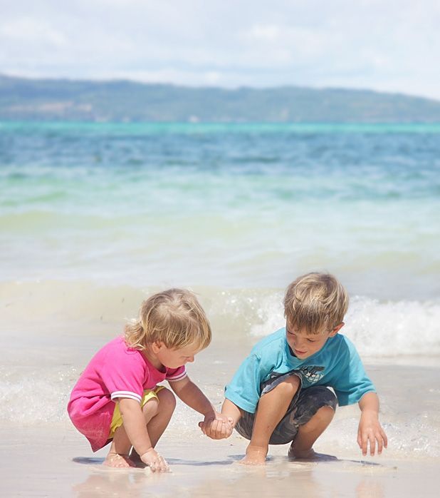 Two children holding hands while crouching on a sandy beach by the ocean. Two children holding hands while crouching on a sandy beach by the ocean.