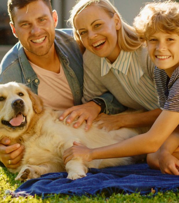 A family and their golden retriever smile while sitting together on a blue blanket on a sunny lawn. A family and their golden retriever smile while sitting together on a blue blanket on a sunny lawn.