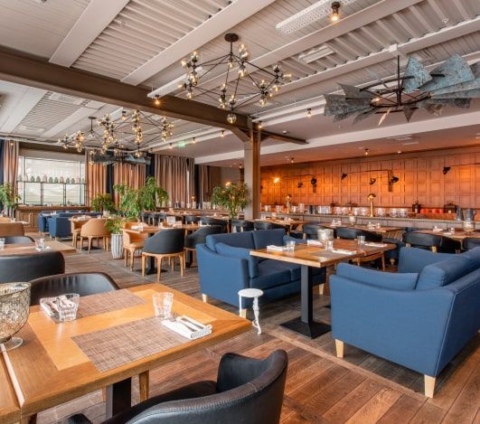 Restaurant interior with wooden floors, blue couches, and tables set for dining. Restaurant interior with wooden floors, blue couches, and tables set for dining.