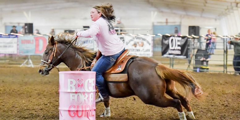 A woman is riding a horse around a pink barrel.