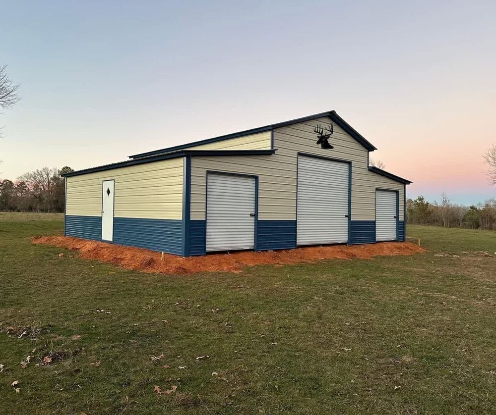 Small cream-and-blue metal barn with roll-up doors on a grassy field at sunset