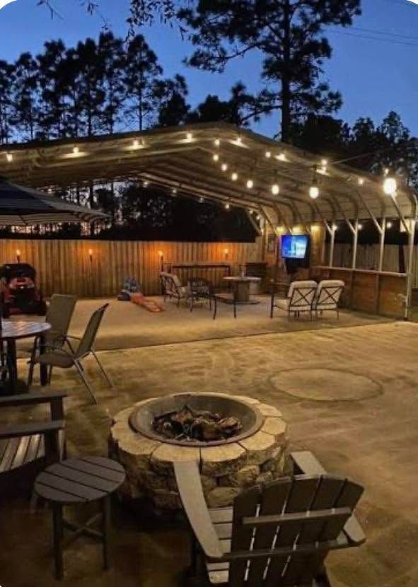 Outdoor patio with fire pit, string lights, and seating under a wooden pergola at dusk