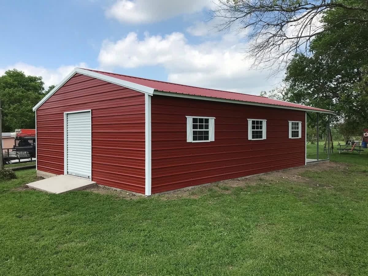 Red metal storage shed with white trim and a roll-up door in a grassy yard