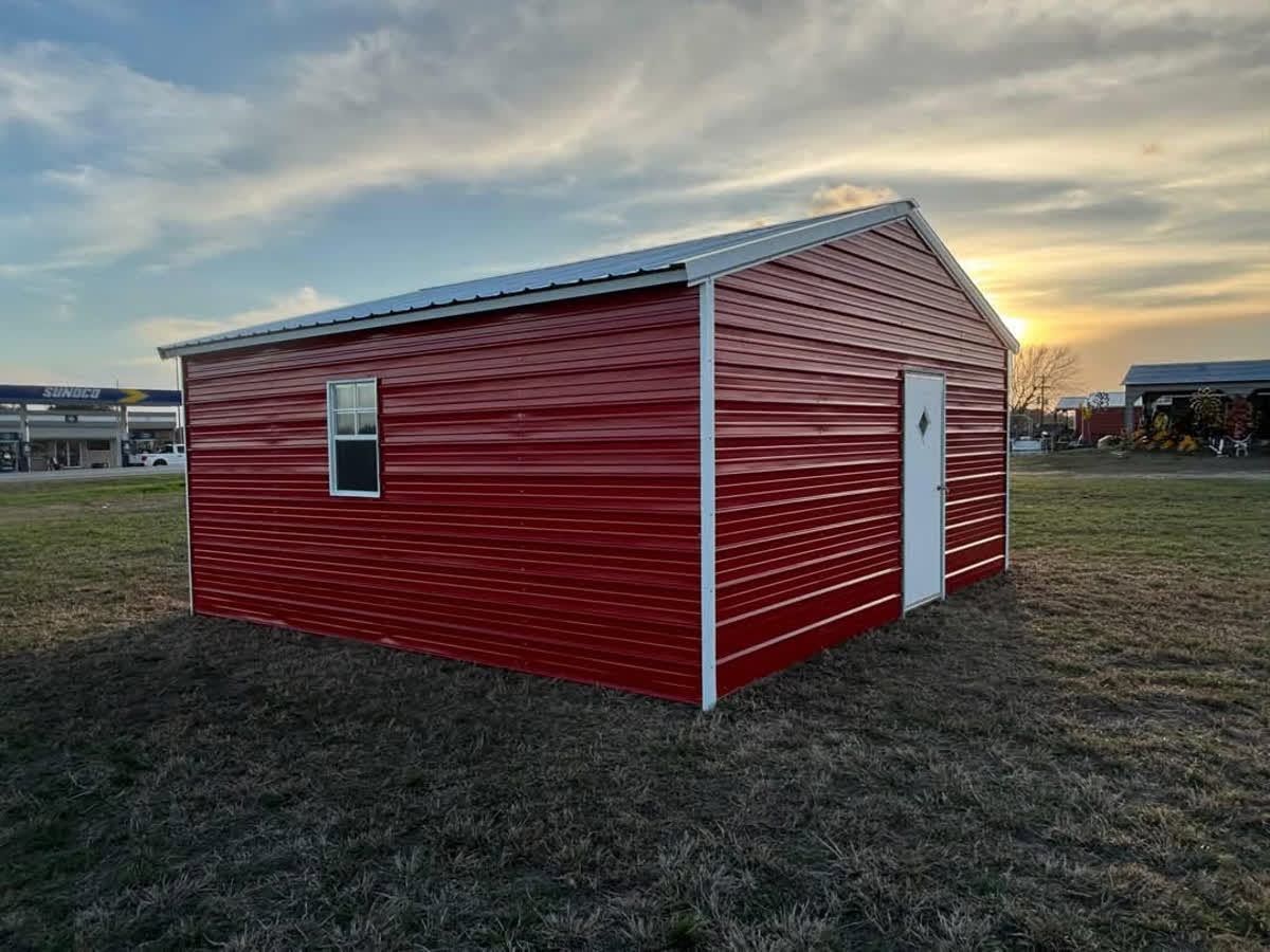 Red metal shed with white trim on a grassy field at sunset.