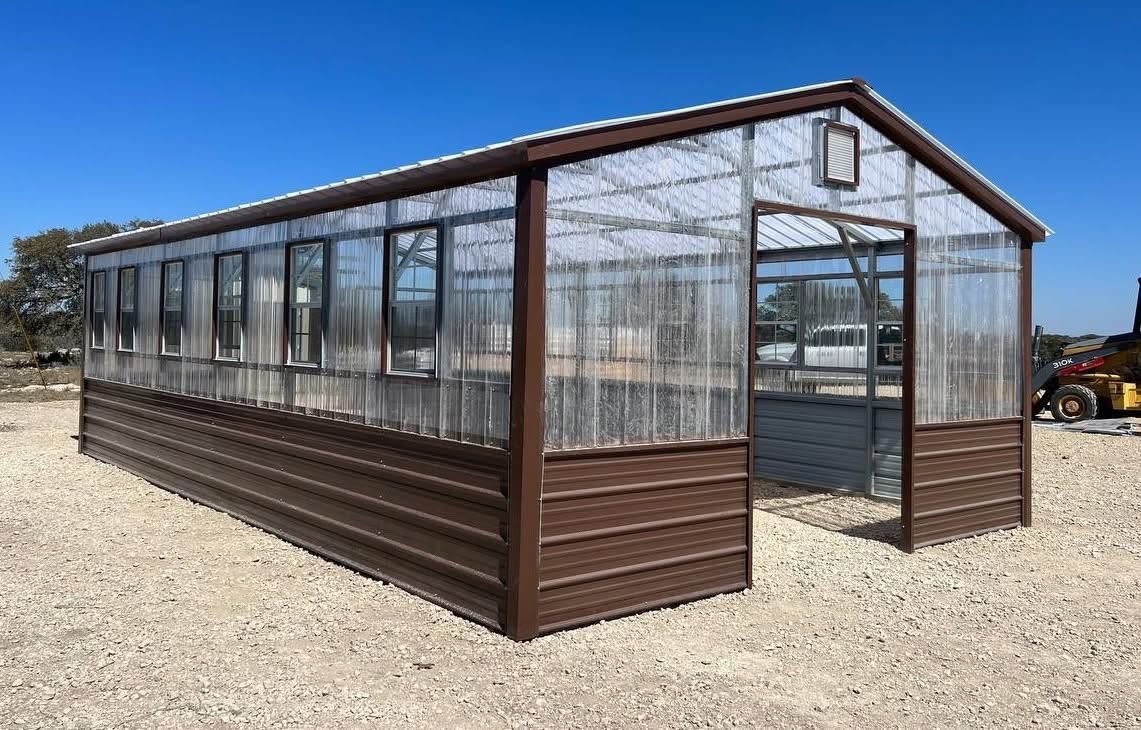 Metal-framed greenhouse with transparent walls on a gravel lot under a clear sky
