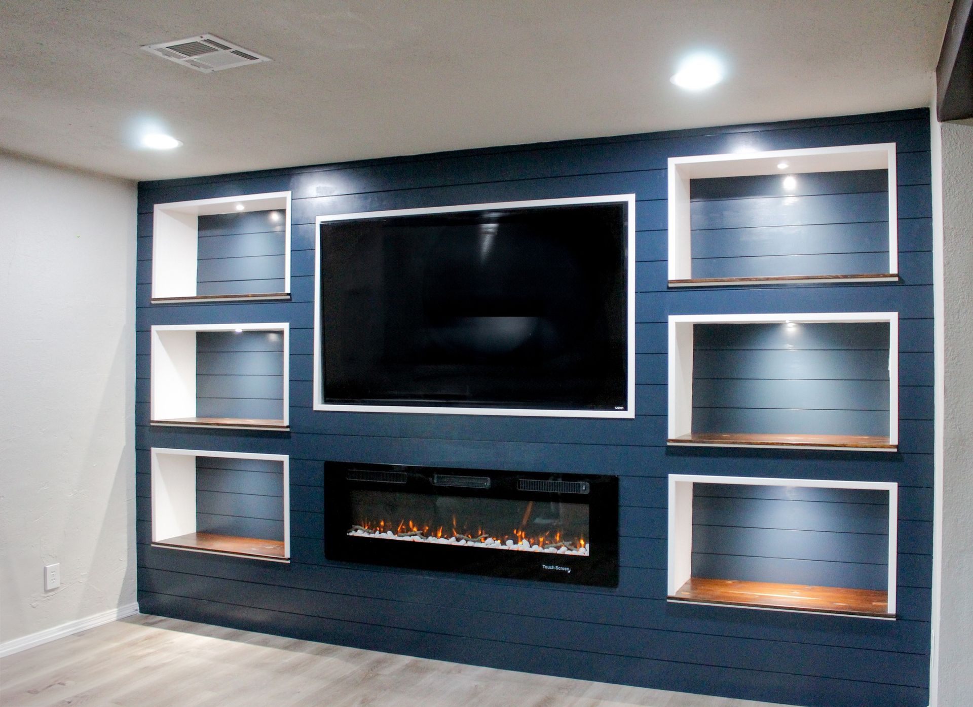 Built-in entertainment center with blue shiplap, shelves, fireplace, and mounted TV.