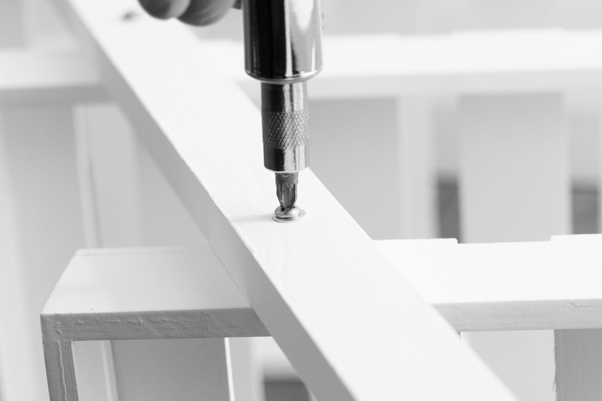 A person using a screwdriver to fasten a screw into a white wooden beam.