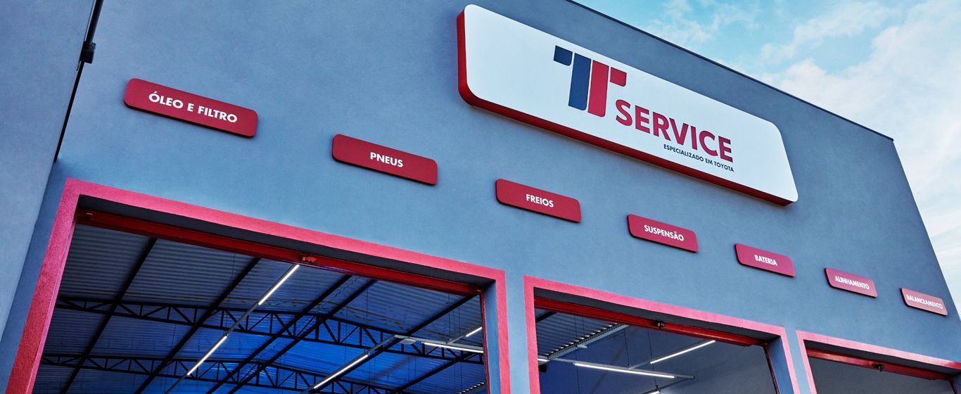 Vista externa da oficina mecânica "T Service", com sinalização vermelha e cinza.