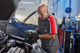 Um mecânico em uma oficina trabalha em um carro. Ele está segurando uma bateria preta.