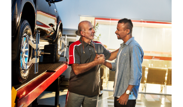 Mecânico de automóveis aperta a mão de um cliente em uma oficina mecânica ao lado de um carro.