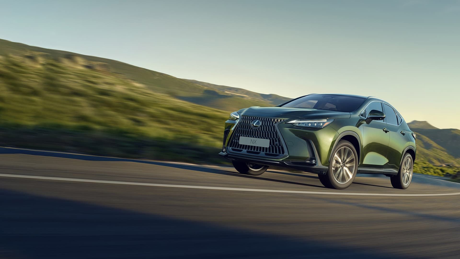 SUV Lexus verde trafegando por uma estrada sinuosa com uma colina gramada ao fundo.