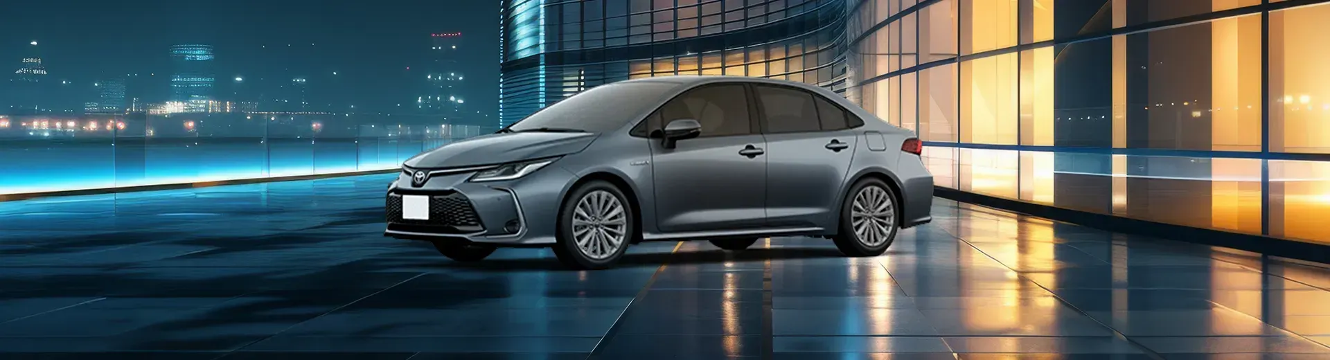 Um Toyota Sedan cinza estacionado em frente a um moderno prédio de vidro à noite.