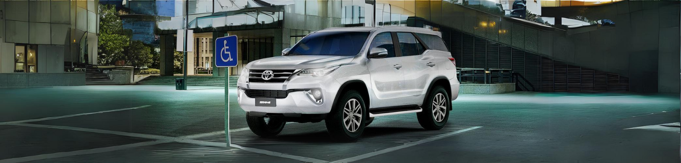 Um SUV branco estacionado em uma vaga reservada para deficientes à noite. A placa azul de deficiente é visível.