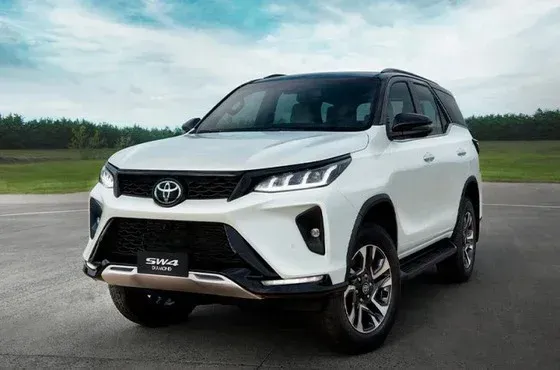 SUV Toyota Fortuner branca estacionada em uma estrada asfaltada, com detalhes em preto e céu nublado ao fundo.
