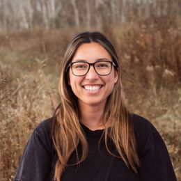 Smiling person with glasses standing outdoors in a brown grassy field