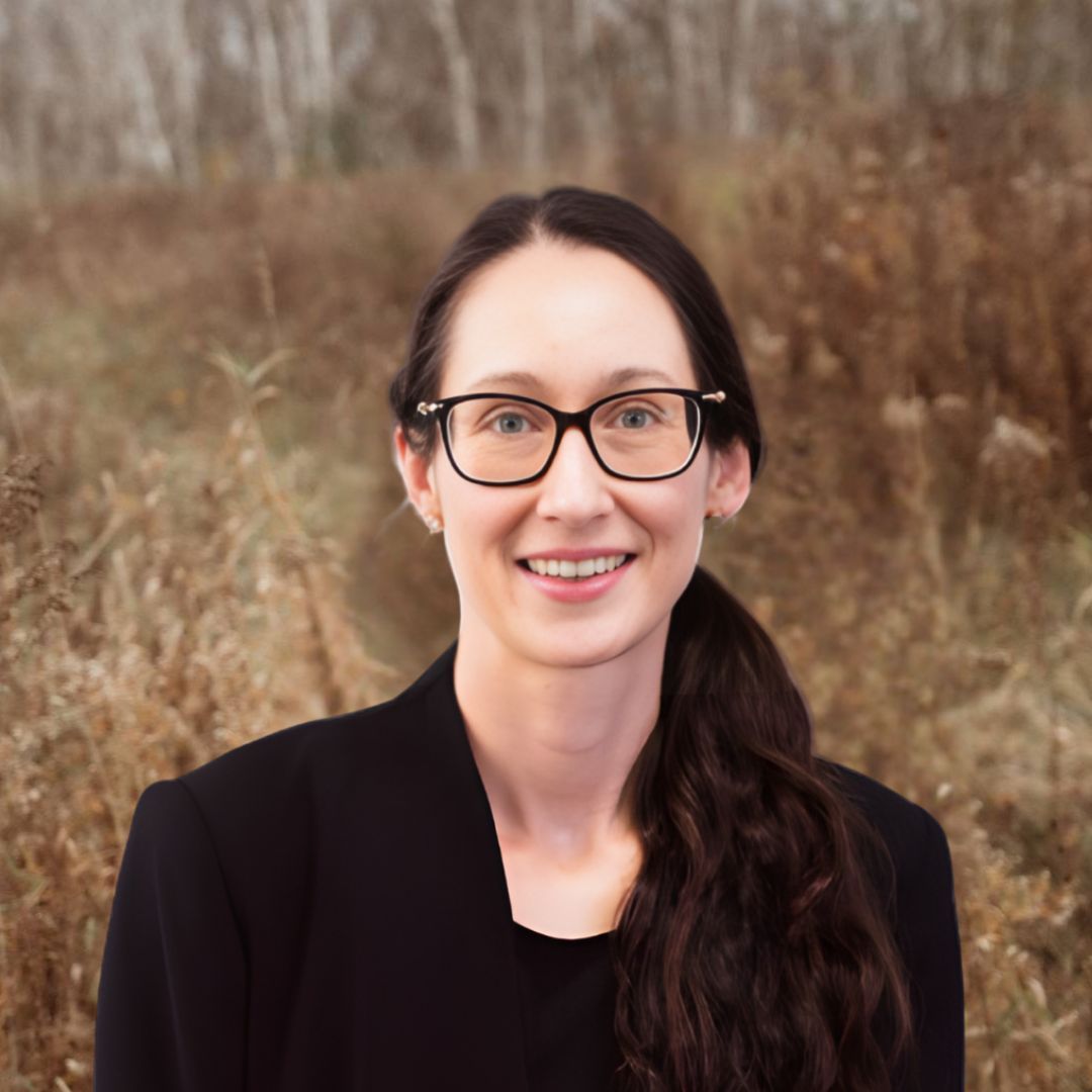 A woman wearing glasses and a black jacket is smiling for the camera.