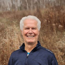 Smiling person in a navy jacket standing outdoors in a brown field