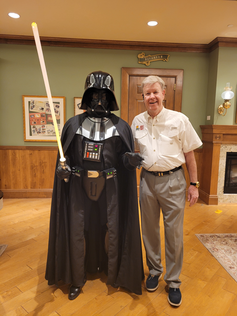 A man is standing next to a darth vader costume holding a light saber.