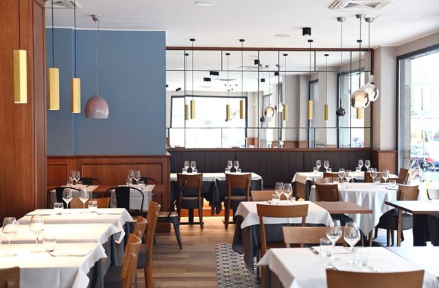 Elegante interno del ristorante con tavoli apparecchiati per la cena, palette di colori neutri, dettagli in legno e vetro.
